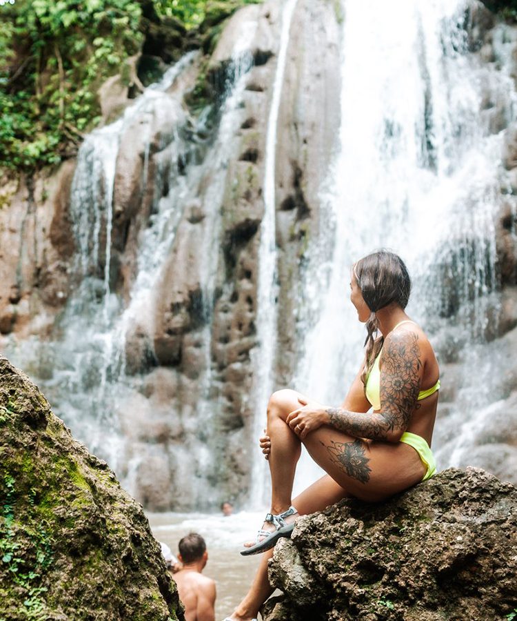 A woman sitting on the rocks near a waterfall.