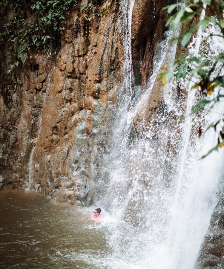 A person swimming in the water near a waterfall.