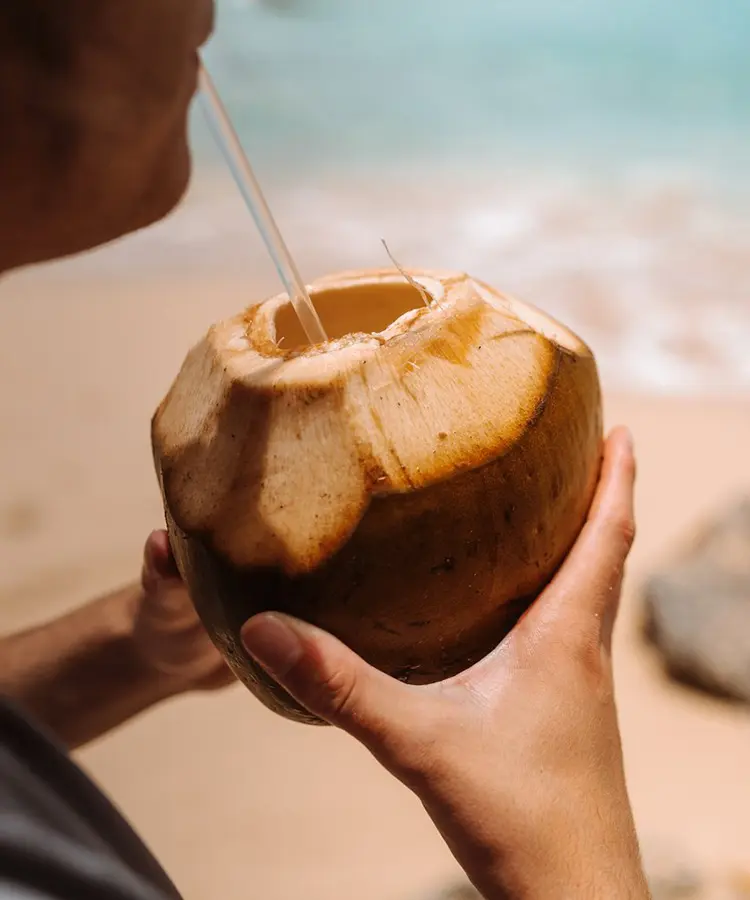 A person holding an open coconut on the beach