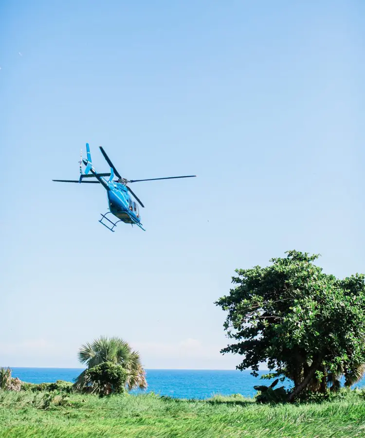 A helicopter flying over the ocean with trees in the background.