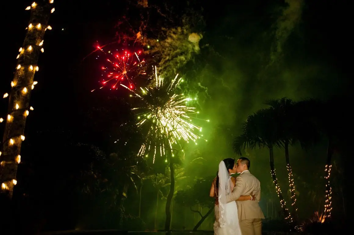 A bride and groom kissing in front of fireworks.
