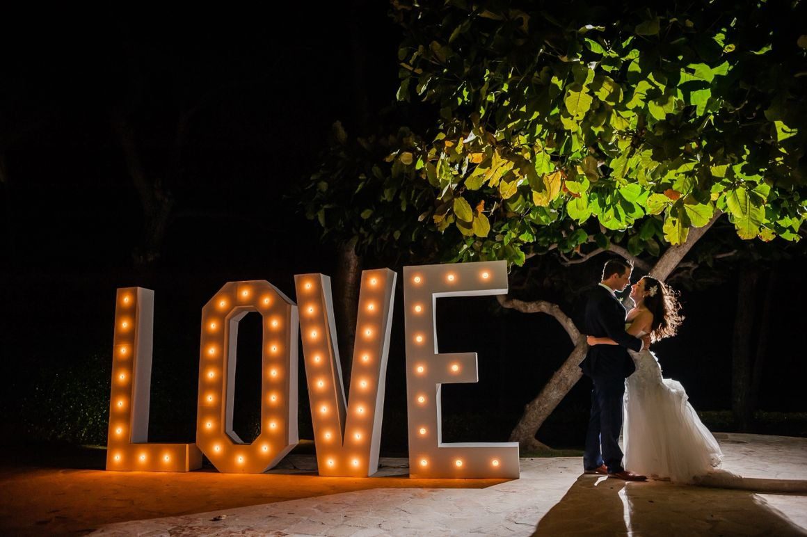 A couple standing next to the word love lit up with lights.