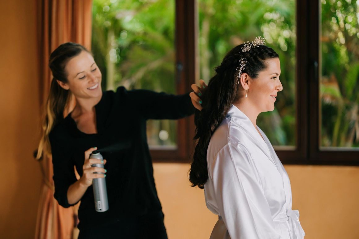 A woman is spraying another woman 's hair.
