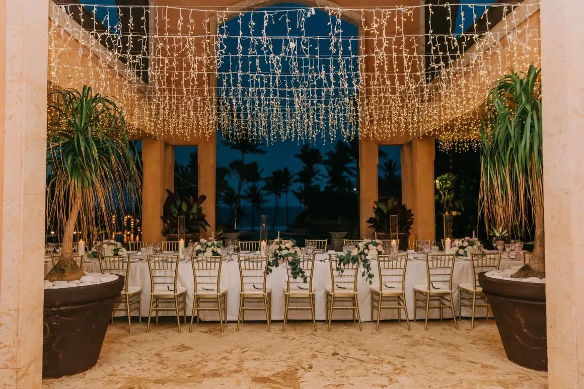 A long table with many chairs and lights hanging from the ceiling.