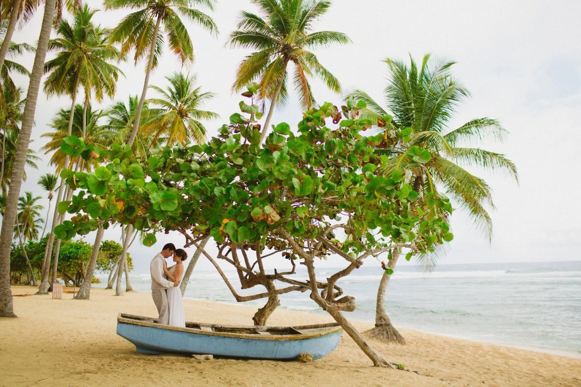 A couple is standing on the beach in their boat.